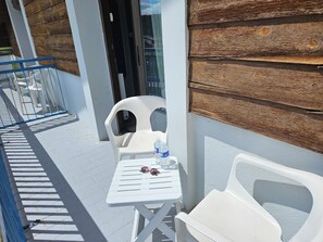 A balcony with white plastic chairs and a table, a bottle of water, and sunglasses on the table.