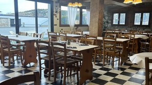 Un restaurante con mesas y sillas de madera, piso a cuadros y ventanas amplias con cortinas.