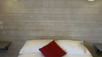 A bed with white bedding and a red pillow, two bedside tables, and wall-mounted lights on a wooden wall.