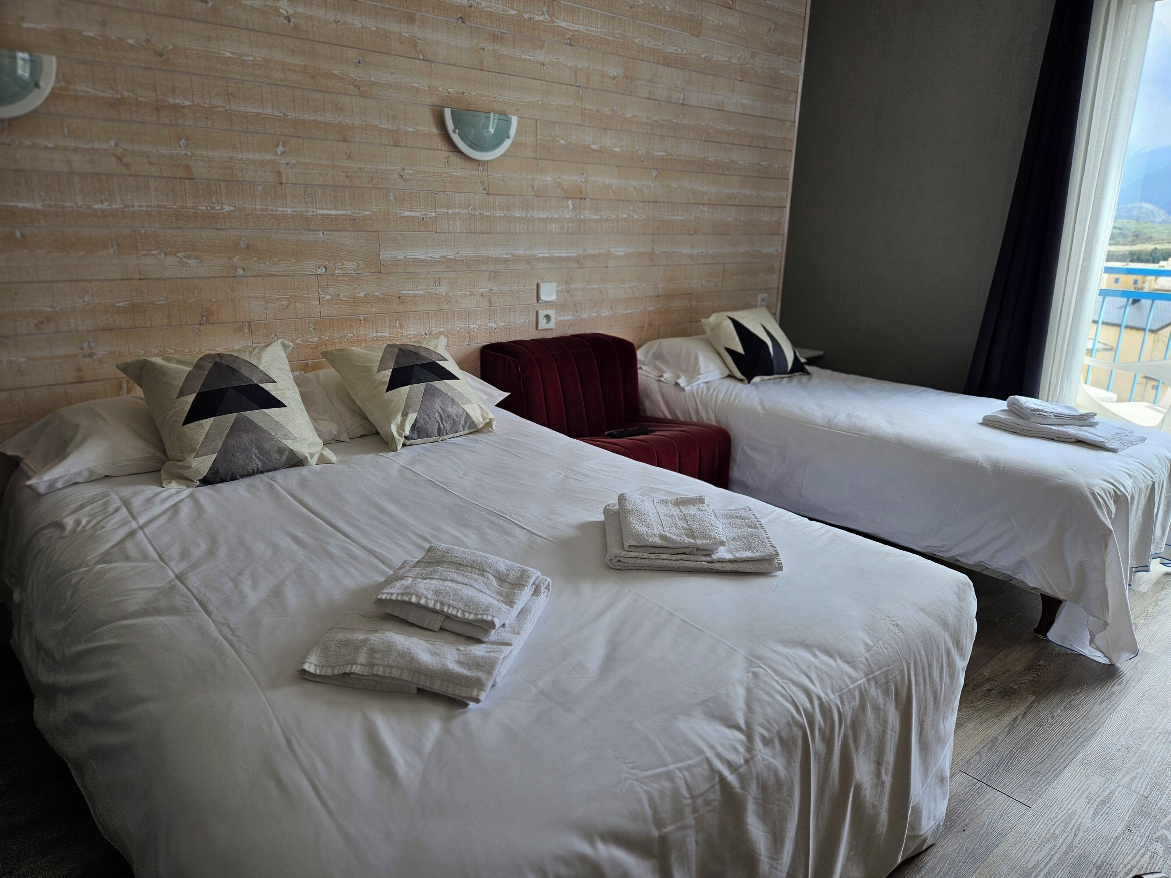 Ein Hotelzimmer mit zwei Betten, jeweils mit weißer Bettwäsche und Kissen, einer Holzwand und einem Fenster mit Blick.