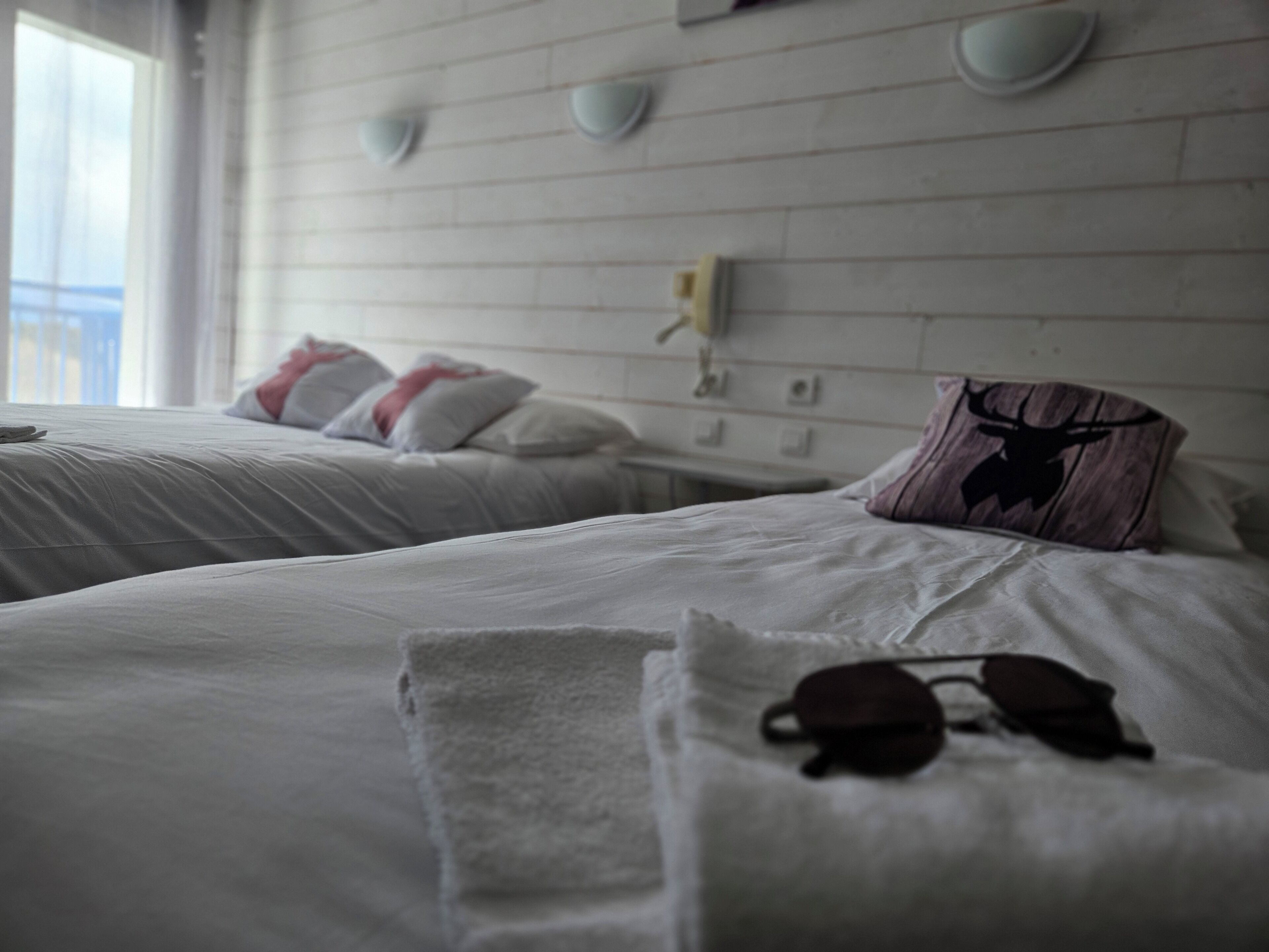 A hotel room with two beds, each with white bedding and pillows, a towel, and a pair of sunglasses on one bed.