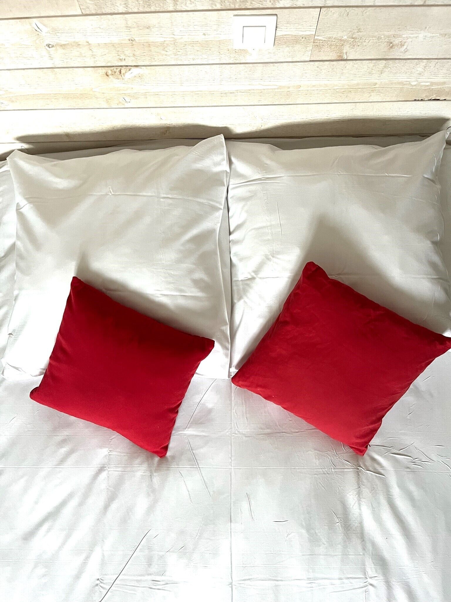 Ein Bett mit weißer Bettwäsche und zwei roten Kissen.