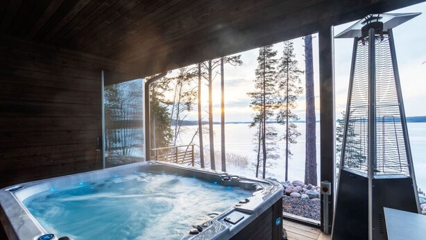 A hot tub with a wooden deck and a view of a lake and trees. - Saunamäki Resort - Seafront Luxury (Salo)