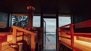 A sauna room with wooden benches and a large window overlooking a wooden deck. - Saunamäki Resort - Seafront Luxury (Salo)