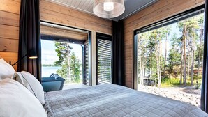 A bedroom with a large bed, a view of trees and a body of water through open windows. - Saunamäki Resort - Seafront Luxury (Salo)
