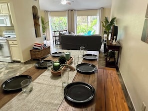 A dining area with a wooden table set for six, a sofa, and a kitchen in the background. - Tropical paradise huge yard 2 min walk 2 beach dogs (South Padre Island)