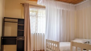 Ein Schlafzimmer mit einem hölzernen Bett, einem Schreibtisch mit Stuhl und einem Fenster mit durchsichtigen Vorhängen.