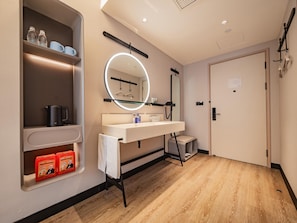 Un baño moderno con tocador, espejo con luz, estante con artículos de aseo y una puerta.
