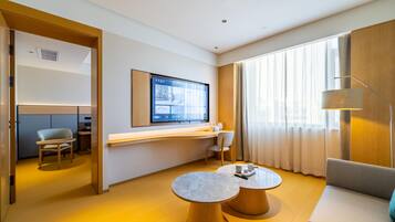 A modern hotel room with a large TV, a sofa, a desk, and a dining area.