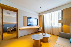 Een moderne hotelkamer met een grote televisie, een bank, een bureau en een zithoek.