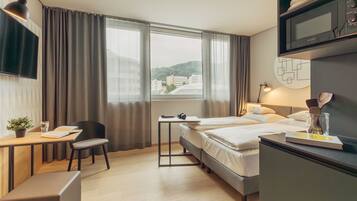 Une chambre d’hôtel avec un lit, un bureau et une chaise, une télévision et une fenêtre avec des rideaux.