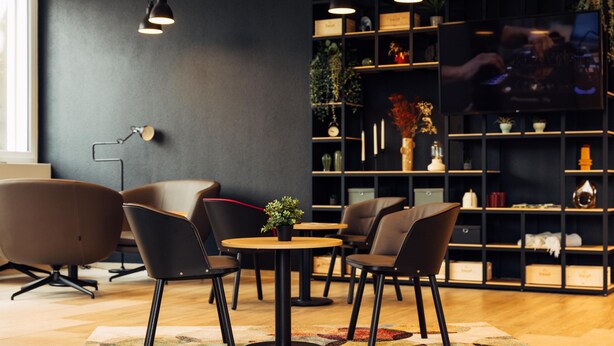 A modern interior with a round table, four chairs, a bookshelf, and a television. - Harry's Home Zürich Limmattal (Spreitenbach)