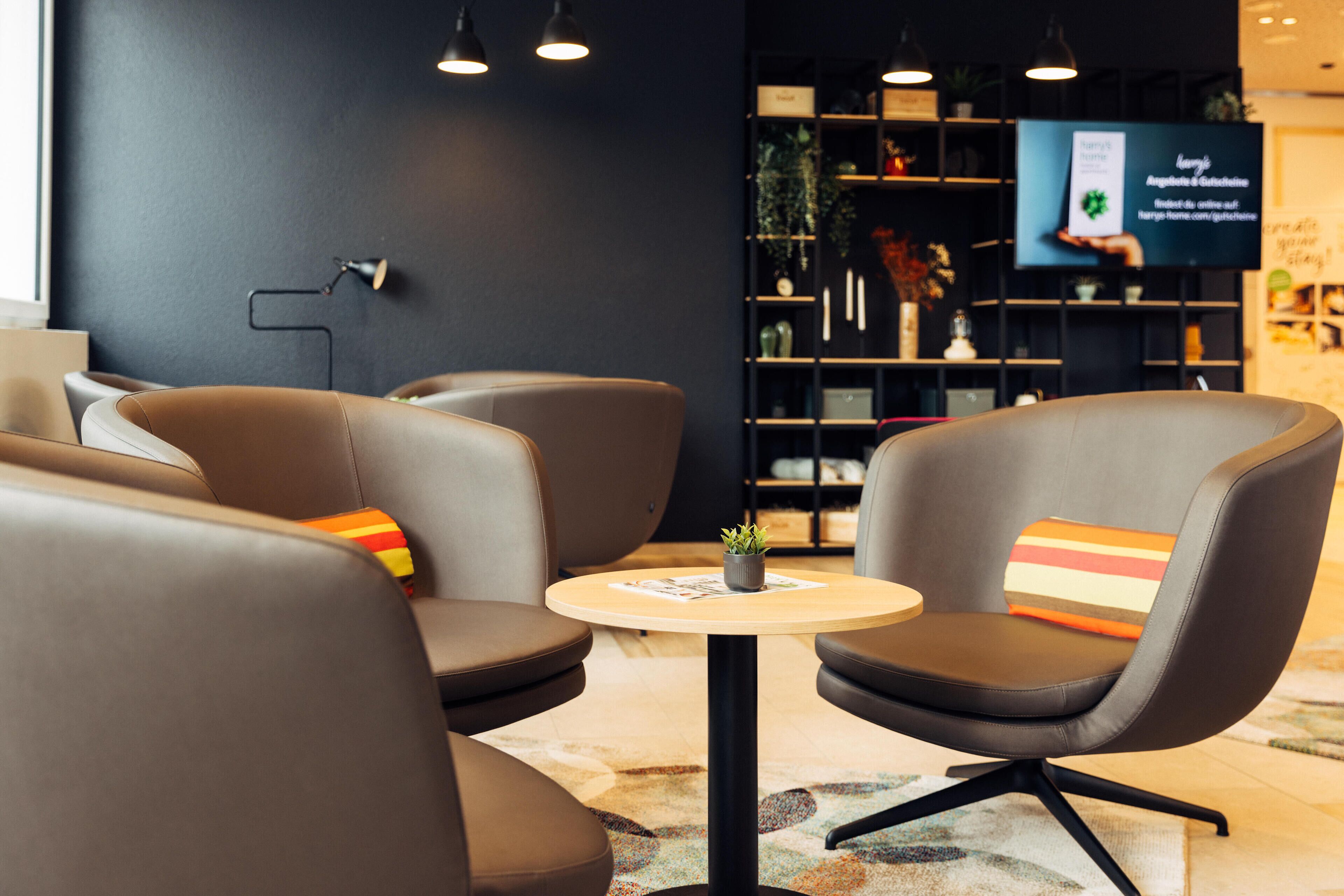 Un espace de détente moderne avec des fauteuils en cuir, une petite table ronde et un écran de télévision en arrière-plan.