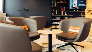 A modern lounge area with leather chairs, a small round table, and a television screen in the background. - Harry's Home Zürich Limmattal (Spreitenbach)
