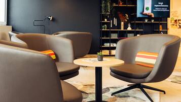 Un espace de détente moderne avec des fauteuils en cuir, une petite table ronde et un écran de télévision en arrière-plan.