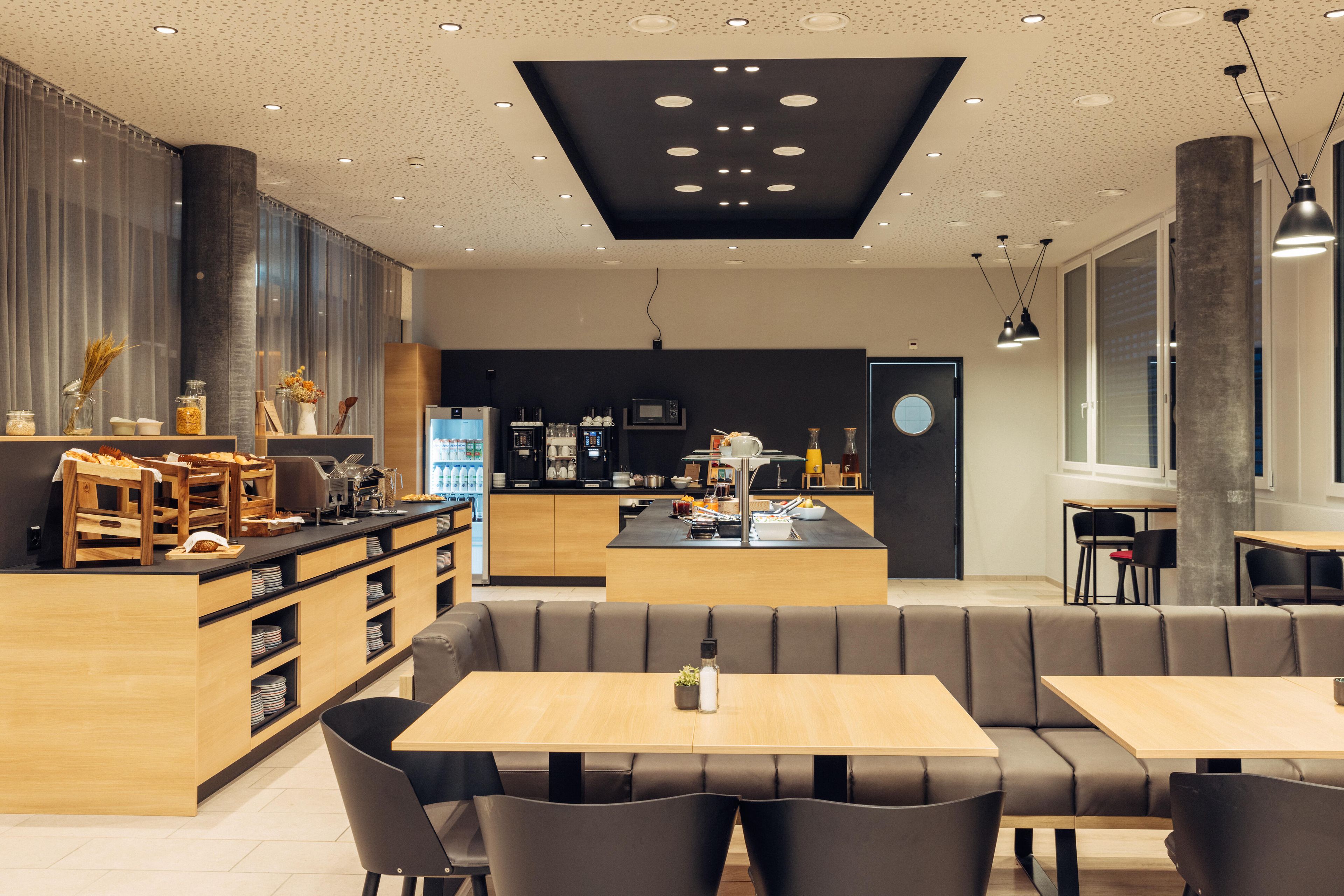A modern restaurant with a central island, seating area, and kitchen in the background.