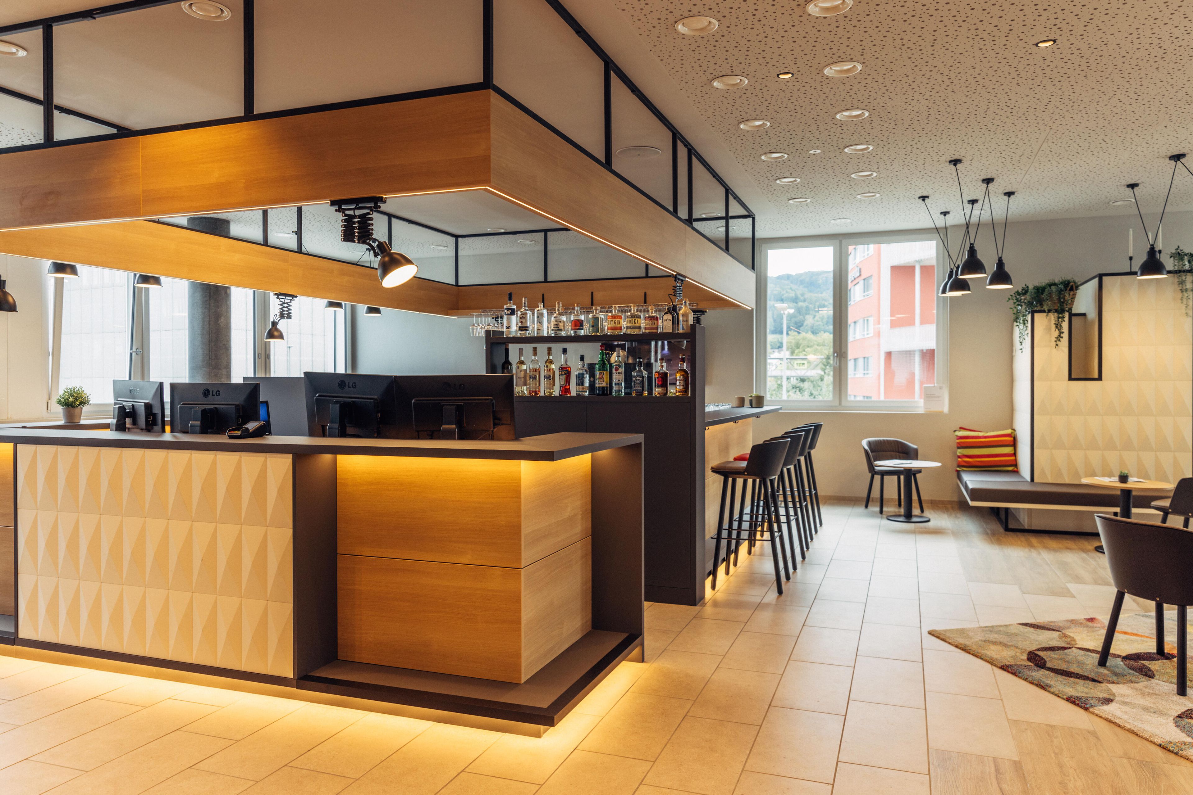 Een moderne bar met een houten toonbank, barstoelen en een zithoek met een bank en stoelen.