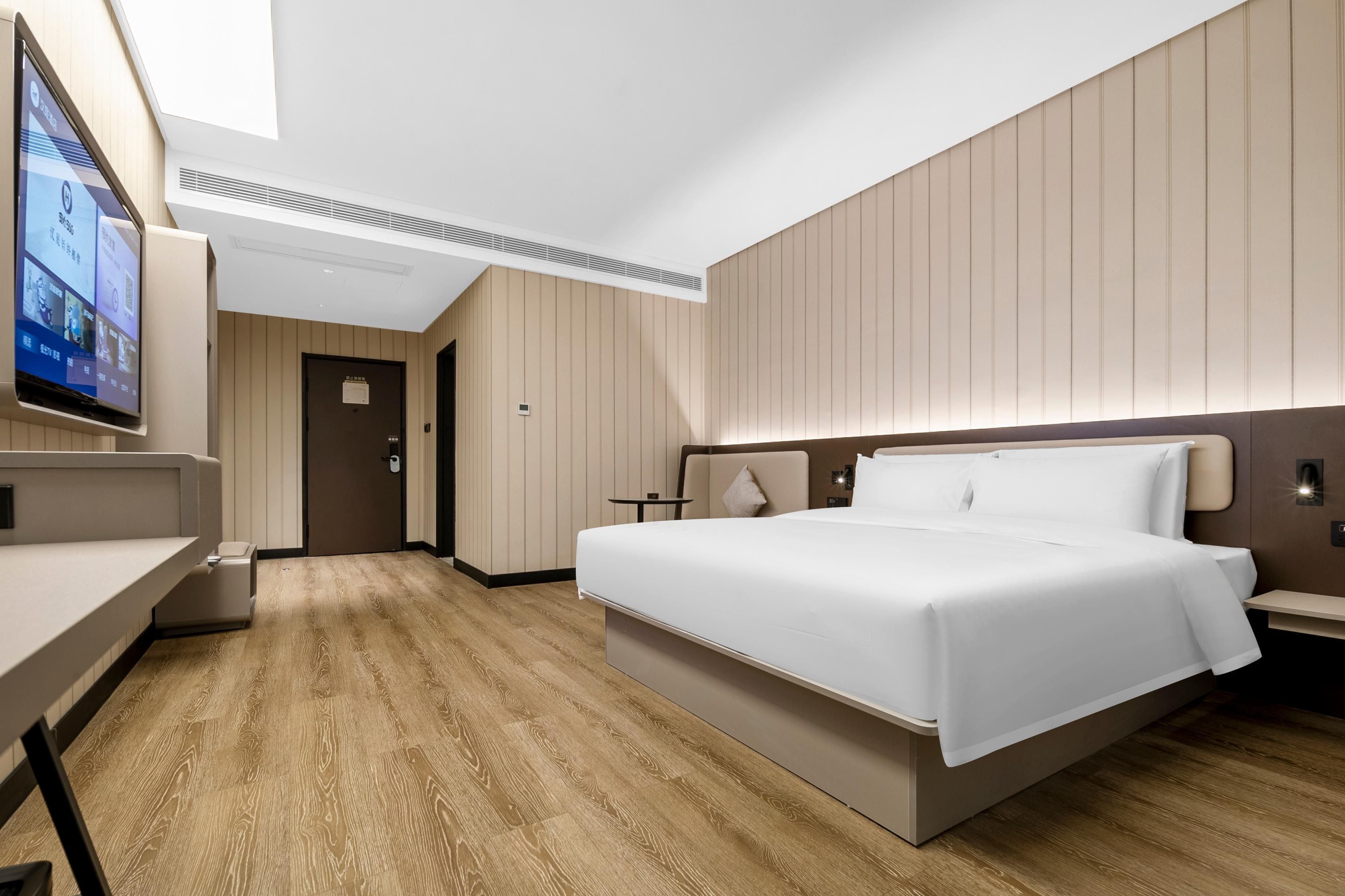 Una habitación de hotel moderna con una cama grande, un escritorio, televisión y piso de madera.