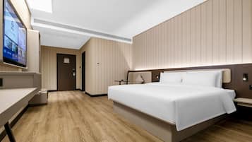 Una habitación de hotel moderna con una cama grande, un escritorio, televisión y piso de madera.
