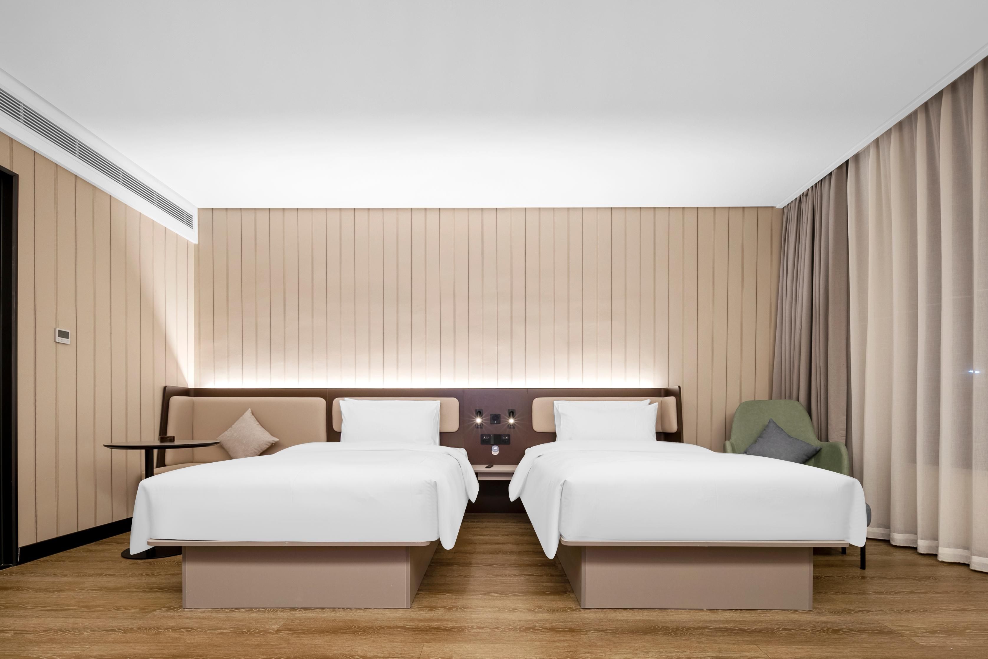 Habitación de hotel con dos camas, una mesita, una silla y un panel de control en la pared.