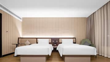 Habitación de hotel con dos camas, una mesita, una silla y un panel de control en la pared.