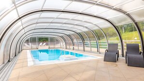 A covered swimming pool with a glass ceiling, lounge chairs, and a view of the outdoors. - Hotel Solina Resort & Spa (Solina)