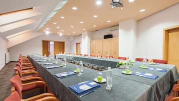 A conference room with a long table, red chairs, and a projector on the ceiling.
