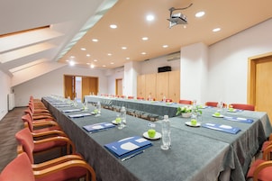 Un salón de conferencias con una larga mesa, sillas rojas y un proyector en el techo.