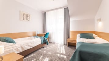 A hotel room with two beds, a desk, a chair, a window with curtains, and a wall-mounted artwork.
