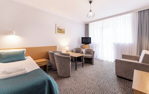 Een hotelkamer met een bed, twee fauteuils, een tafeltje, een televisie en een raam met gordijnen.