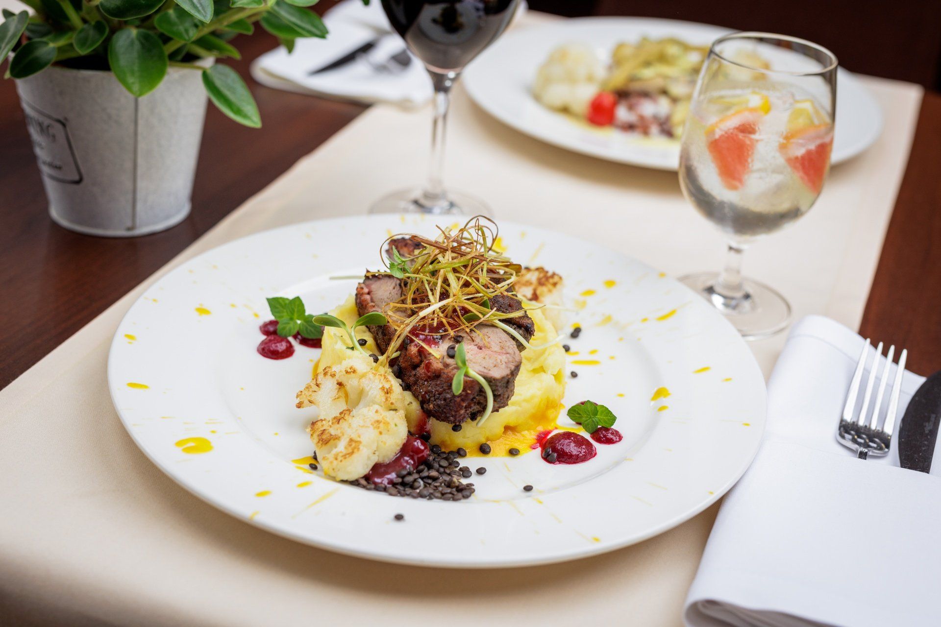 Ein Esstisch mit einem Teller Essen, einem Glas Rotwein und einer Topfpflanze.