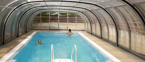 An indoor swimming pool with a glass ceiling and a person swimming.