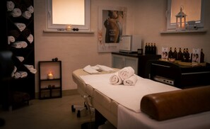Un cuarto de spa con una camilla de masaje, toallas, un estante con botellas y un cartel en la pared.