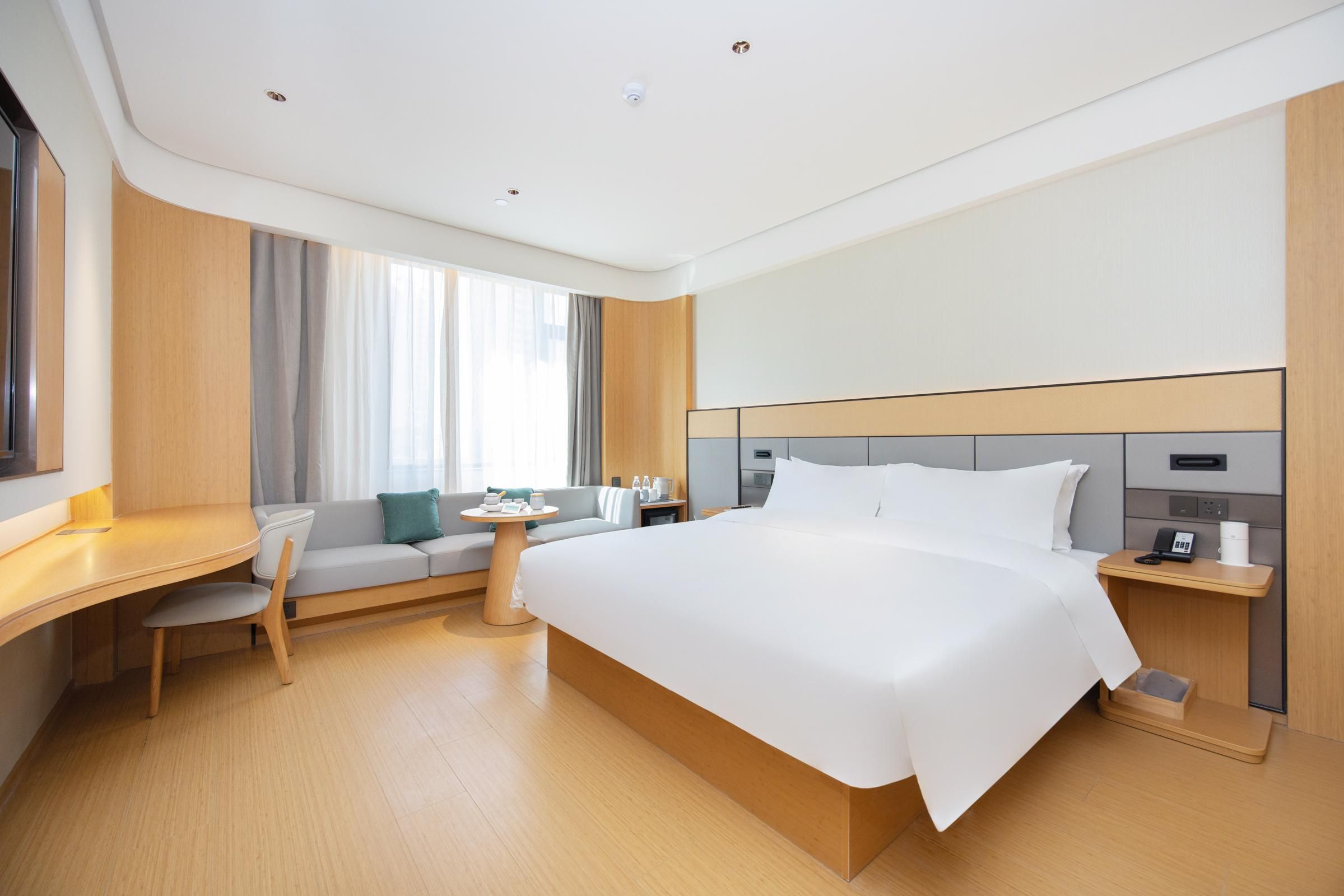 A modern hotel room with a large bed, a desk, a chair, a small table, and a sofa.
