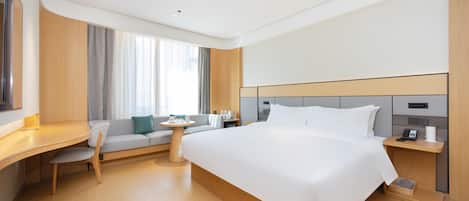 A modern hotel room with a large bed, a desk, a chair, a small table, and a sofa.