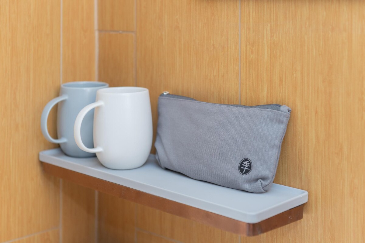 A shelf with two mugs and a grey pouch against a wooden wall.
