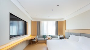 A modern hotel room with a large bed, a desk, a sofa, and a window with curtains.