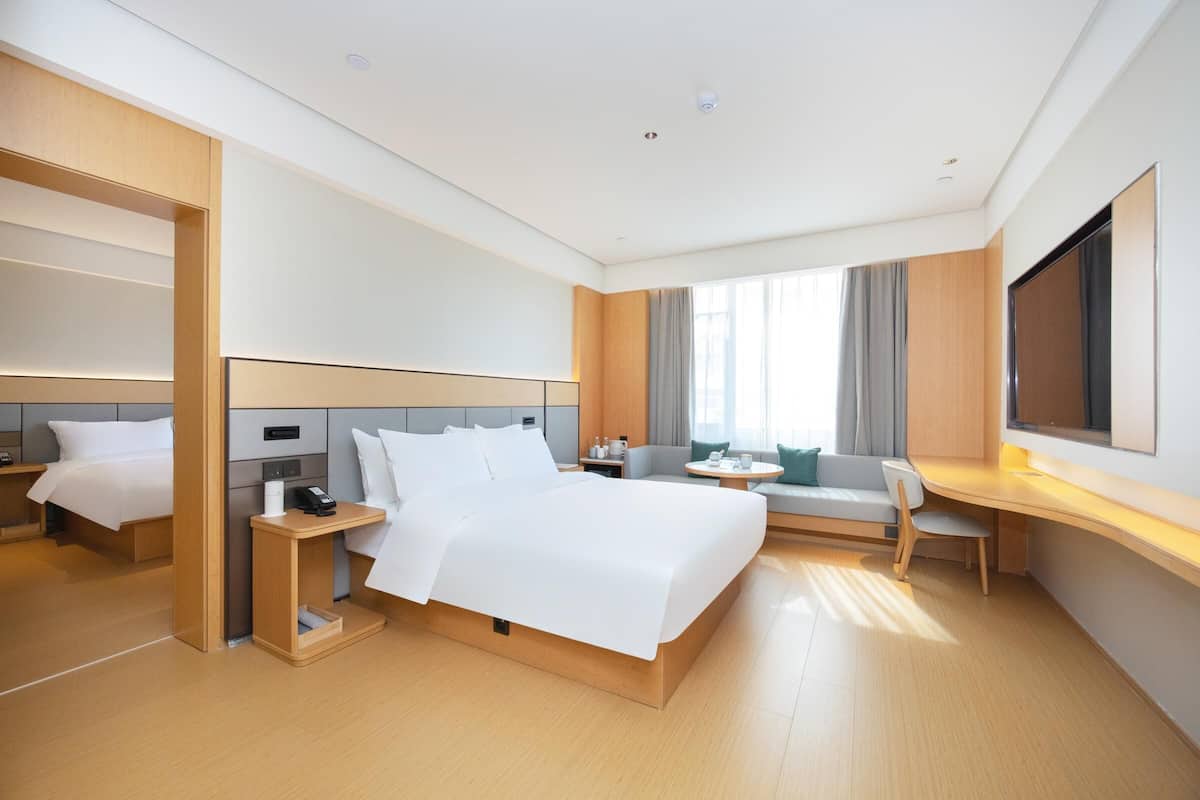 A modern hotel room with a large bed, a desk, a sofa, and a TV.
