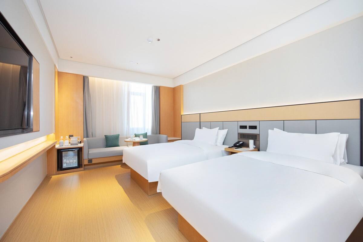 A hotel room with two beds, a sofa, a small table, a nightstand, and a TV.