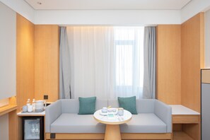 A modern hotel room with a sofa, a small table, a mini-fridge, and a window with curtains. - Ji Hotel Qingdao Xinduxin Changsha Road (Qingdao)