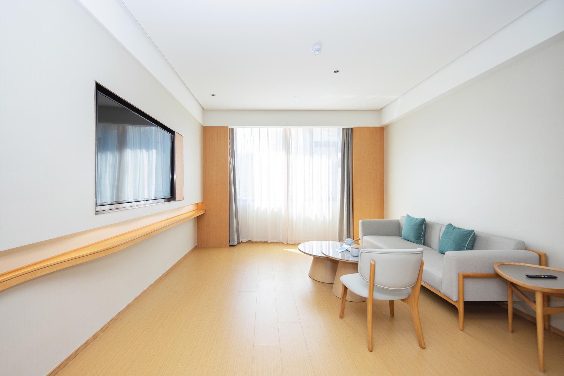 A modern hotel room with a sofa, a small round table, and a TV mounted on the wall.