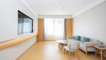Una habitación de hotel moderna con sofá, una mesita redonda y televisor montado en la pared.