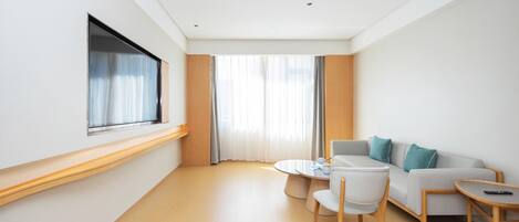 A modern hotel room with a sofa, a small round table, and a TV mounted on the wall.