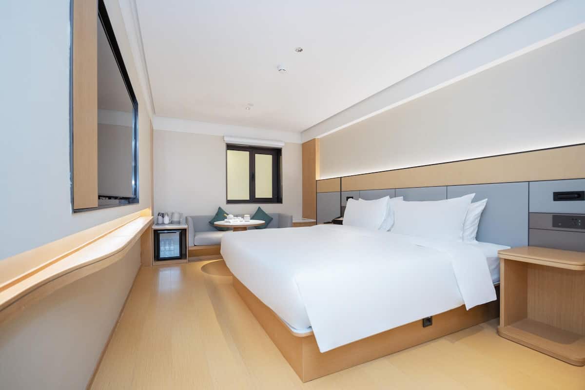 A modern hotel room with a large bed, bedside tables, a small desk, and a window.