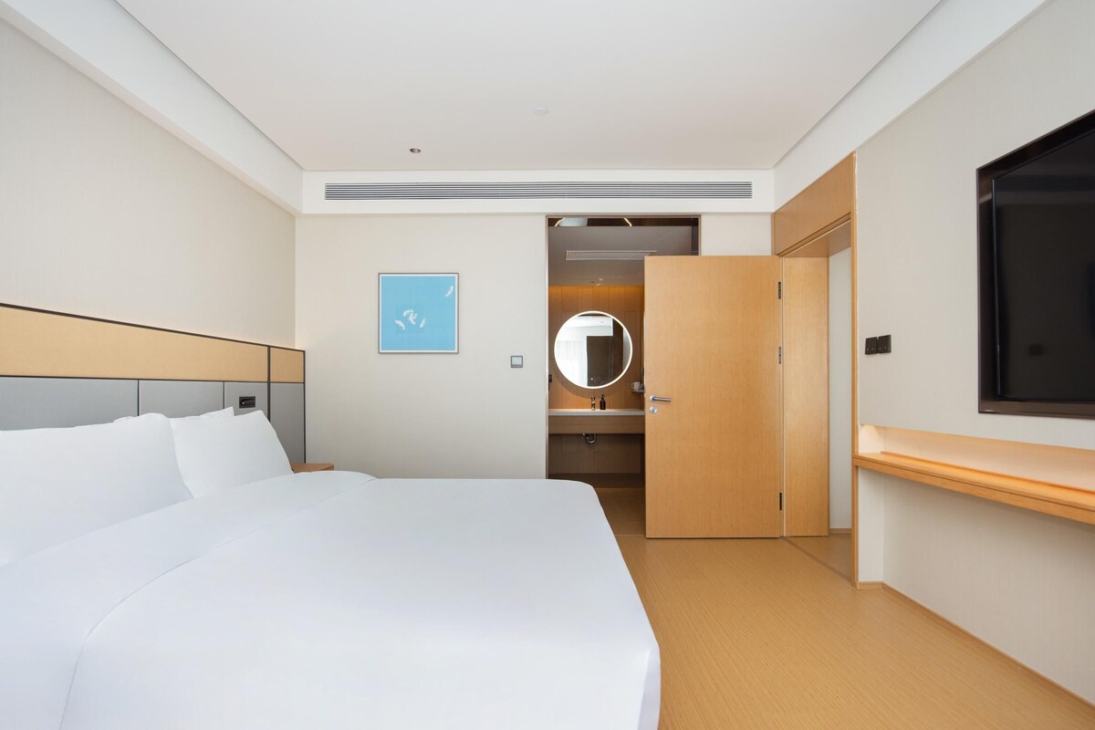 Una habitación de hotel con una cama grande, una mesita de noche, un armario, un espejo y un televisor.