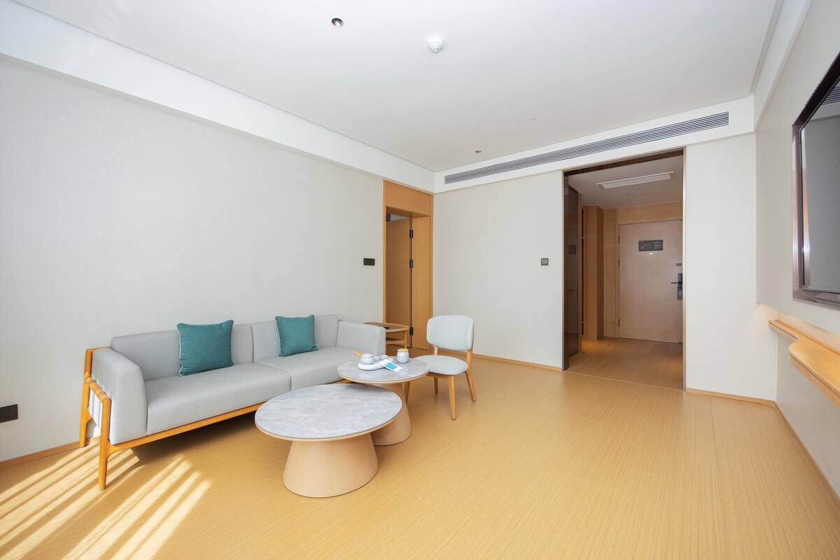 A modern hotel room with a sofa, two round coffee tables, and a chair.