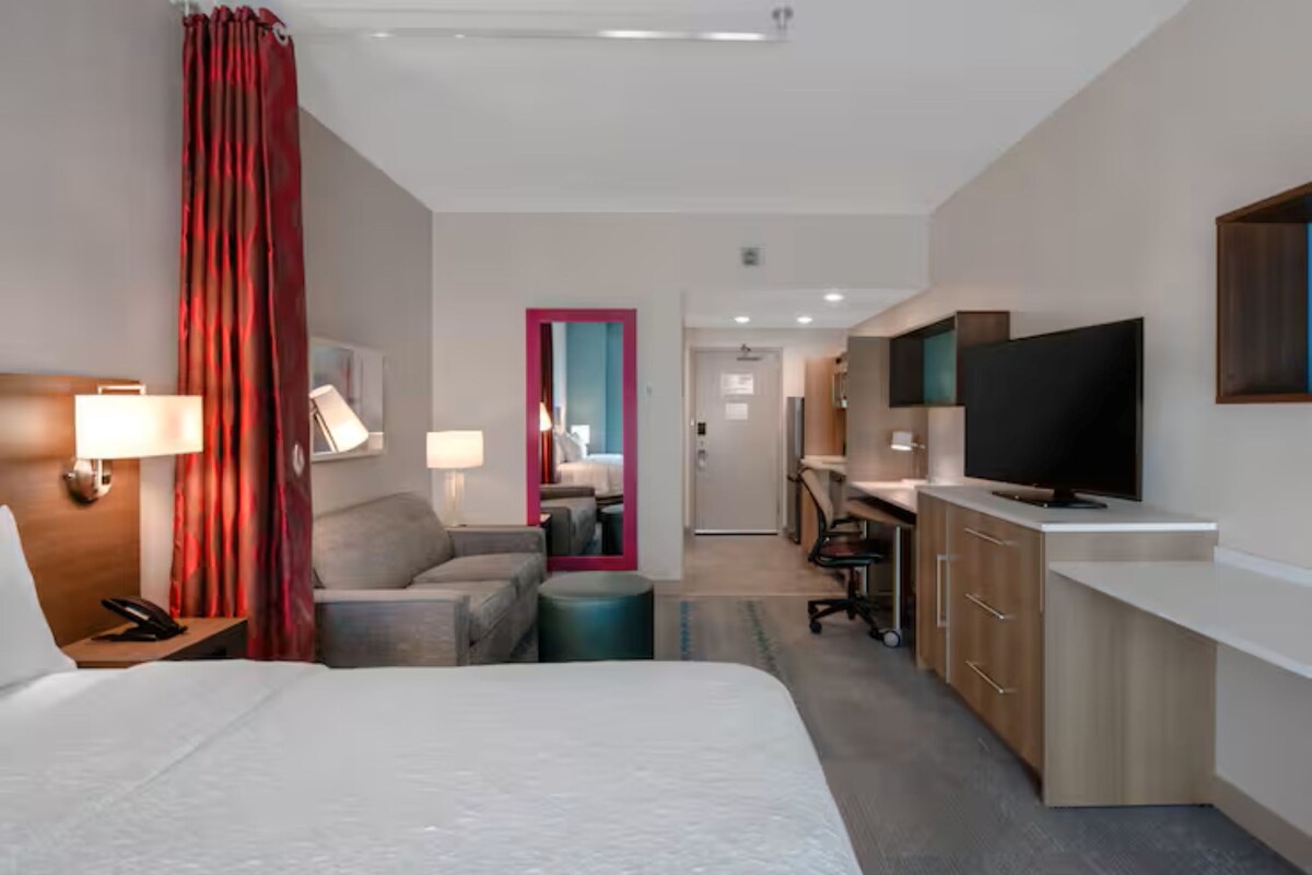 Une chambre d’hôtel avec un lit, un bureau, une télévision et une salle de bain, visibles à travers une porte.