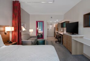 Quarto de hotel com cama, escrivaninha, televisão e banheiro visível por uma porta.