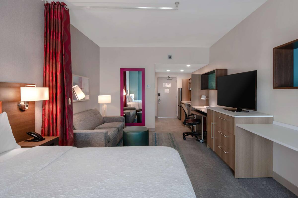 Habitació d'hotel amb un llit gran, dues taules de nit amb làmpades, un escriptori i un televisor de pantalla plana, i un bany visible a través d'una porta.