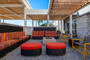 An outdoor patio with wicker furniture, red cushions, and a stone wall backdrop. - Home2 Suites By Hilton Savannah I95 North (Port Wentworth)